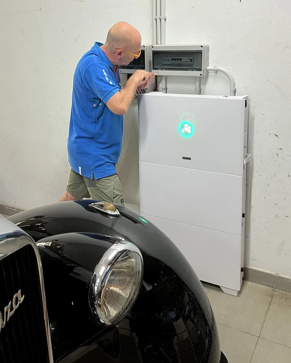 Técnico instalando una batería doméstica en un garaje, junto a un coche